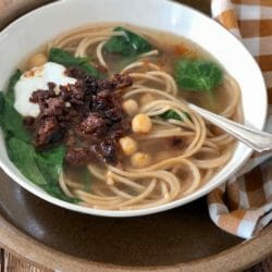 Aush, an Afghan noodle soup with chickpeas, spinach, ground meat, and yogurt with a spoon and checked napkin