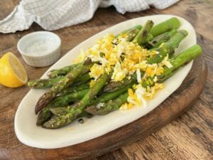 Roasted asparagus with grated egg on a white plate with lemon