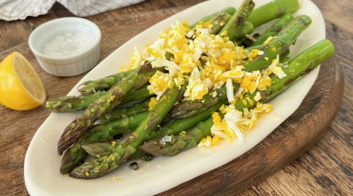 Roasted asparagus with grated egg on a white plate with lemon