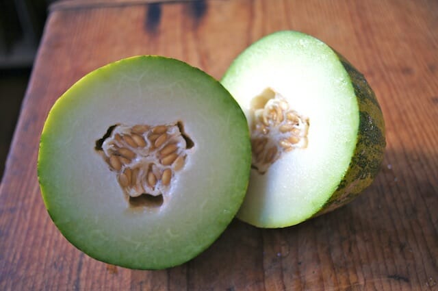 honeydew melon cut in half on a cutting board