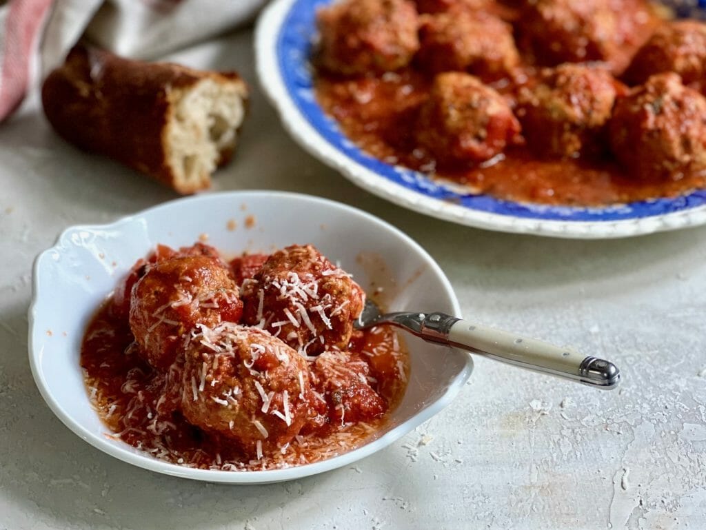 Dish of slow cooker meatballs on a white plate with a fork and crusty bread