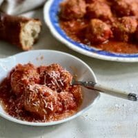 Dish of slow cooker meatballs on a white plate with a fork and crusty bread