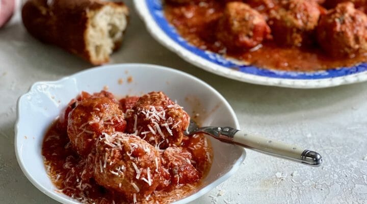Dish of slow cooker meatballs on a white plate with a fork and crusty bread