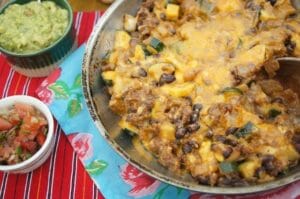 Mexican skillet supper of ground beef and beans topped with cheese in a skillet with colorful Mexican tablecloth and guacamole