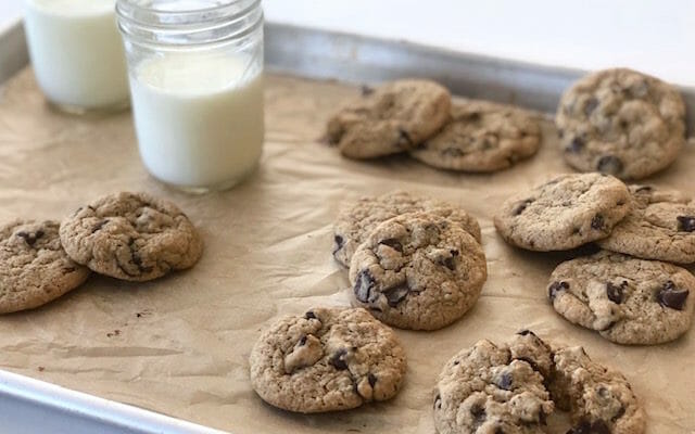 healthier chocolate chip cookies on a baking sheet with glasses of milk