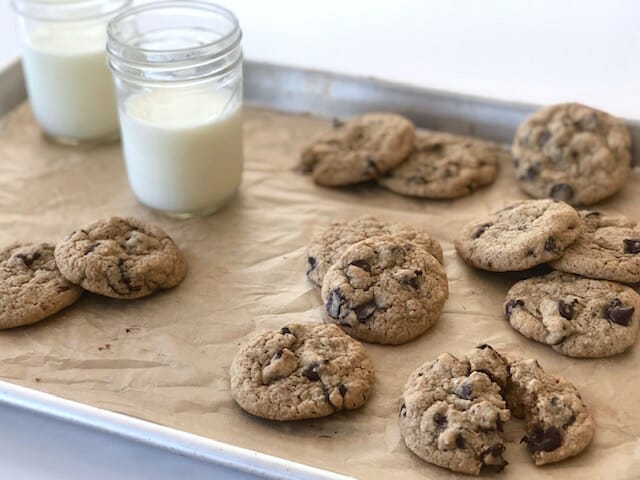 healthier chocolate chip cookies on a baking sheet with glasses of milk
