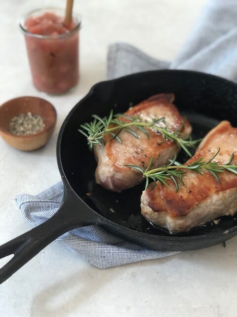 Pork chops in a cast iron skillet with rhubarb compote and rosemary