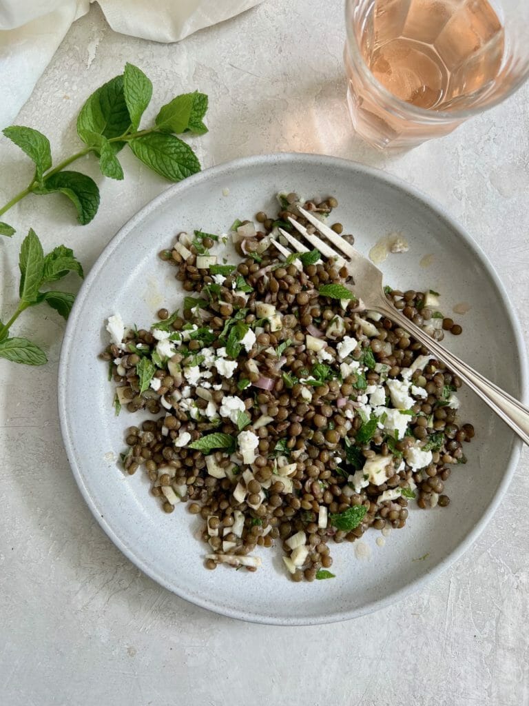 White plate with French Lentil Salad, fork, and glass of rosé