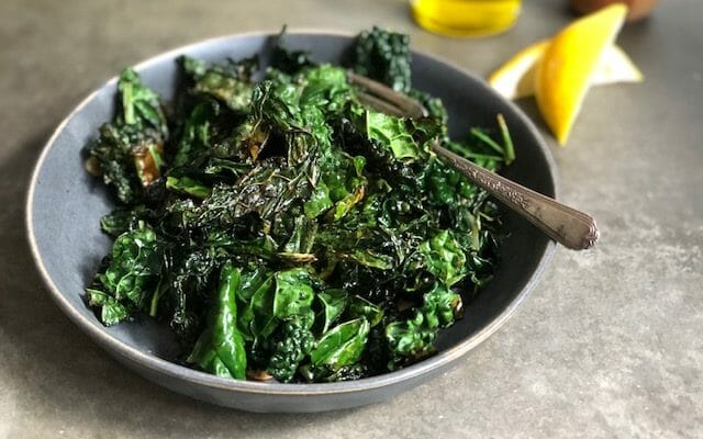 bowl of sauteed kale with olive oil and lemon wedges