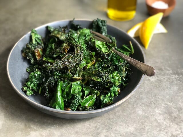 bowl of sauteed kale with olive oil and lemon wedges