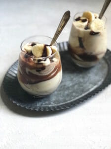 two glasses with butterscotch pudding and a chocolate drizzle with banana on top on a pewter tray