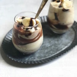 two glasses with butterscotch pudding and a chocolate drizzle with banana on top on a pewter tray