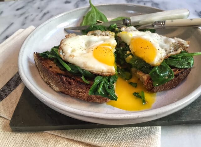 Open faced spinach and egg sandwich on toast with fork and knife