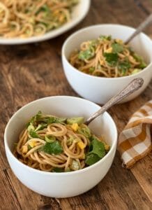 Noodles with peanut sauce and vegetables in white bowls