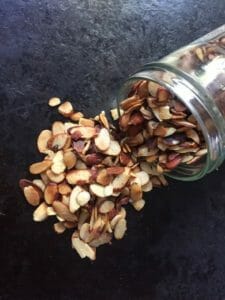 Jar of pan roasted almonds spilling on the counter