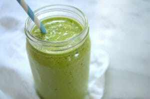 Pineapple kale smoothie in a glass jar with a striped paper straw