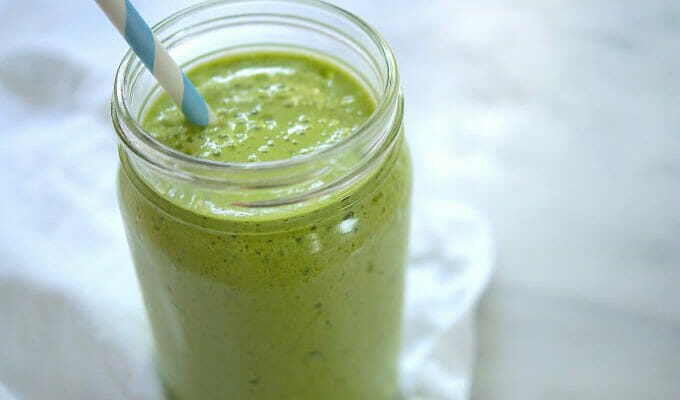 Pineapple kale smoothie in a glass jar with a striped paper straw