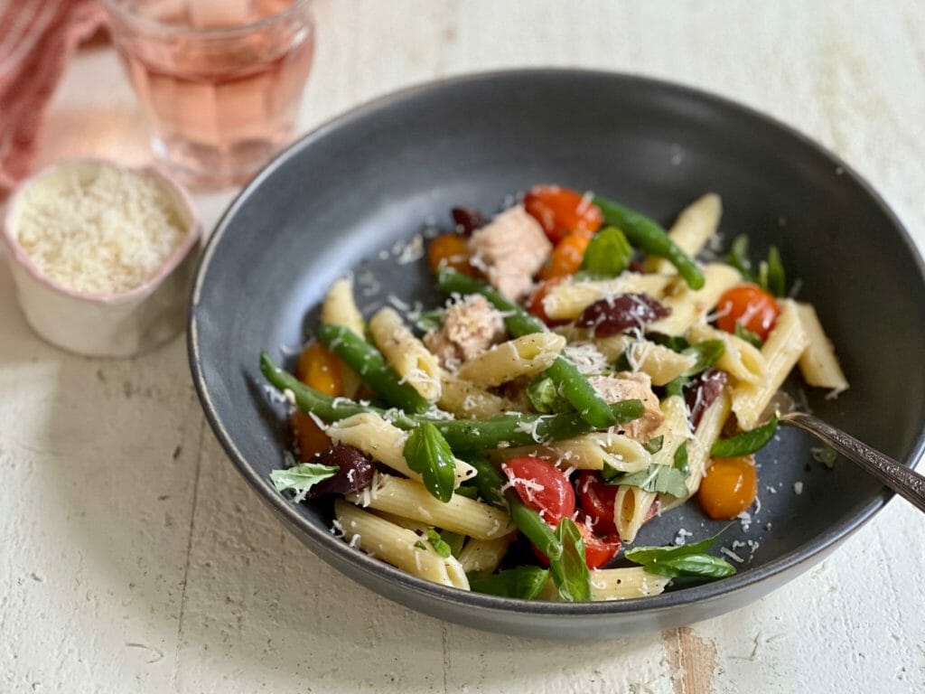 Bowl of nicoise pasta with glass of wine