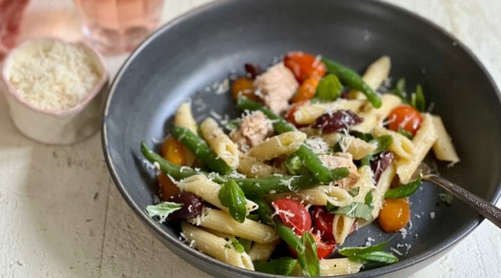 Bowl of nicoise pasta with glass of wine