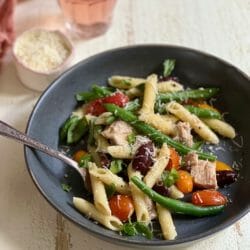 bowl with fork of pasta with beans and tomatoes and tuna with glass of wine