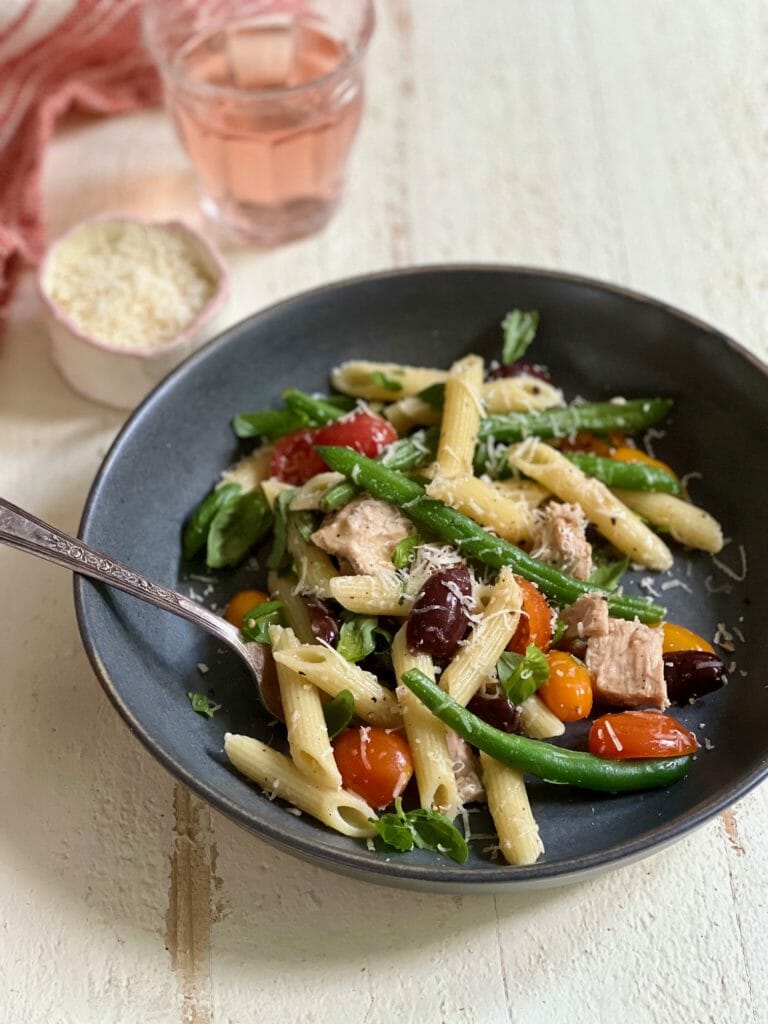 bowl with fork of pasta with beans and tomatoes and tuna with glass of wine