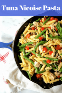 Cast iron skillet with penne, green beans, tomatoes, and tuna with a white and red dishtowel