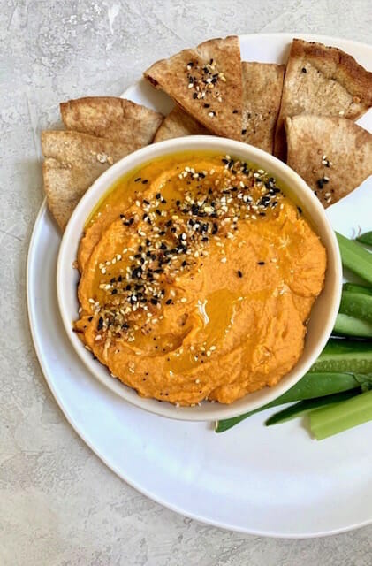 sweet potato hummus in a white bowl with pita chips and vegetables