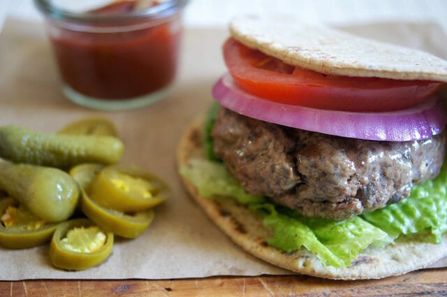 Burger with lettuce, onion, and tomato on a thin bun with pickled jalapenos and ketchup on the side