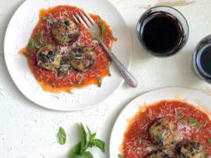 two plates with vegan eggplant meatballs and a glass of red wine