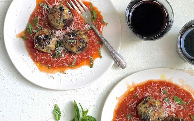 two plates with vegan eggplant meatballs and a glass of red wine