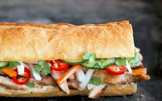 Close up of a chicken banh mi sandwich on baguette with cucumbers, red chiles, and cilantro