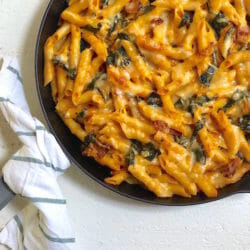 Cast iron pan with a dish towel around the handle and Creamy Baked Pumpkin Pasta with Kale
