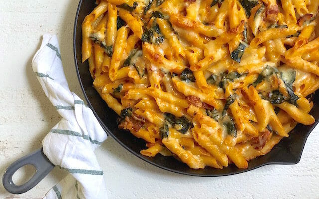 Cast iron pan with a dish towel around the handle and Creamy Baked Pumpkin Pasta with Kale