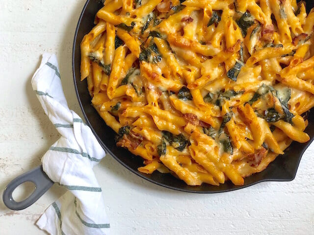 Cast iron pan with a dish towel around the handle and Creamy Baked Pumpkin Pasta with Kale