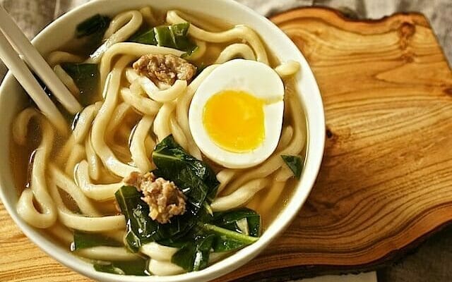 Overhead shot of a bowl of soup with thick udon noodles, greens, and half of a soft cooked egg