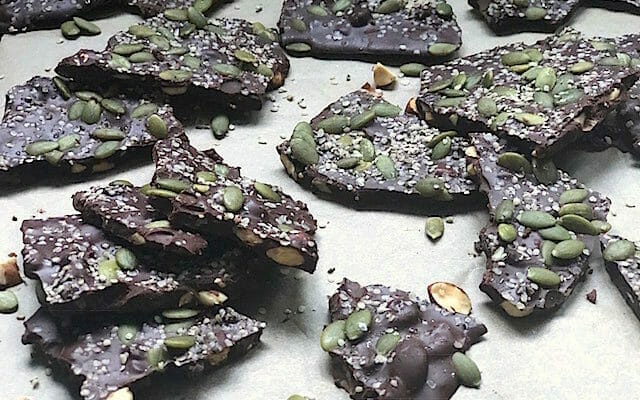 Dark chocolate bark on a sheet pan topped with pumpkin seeds and hemp seeds