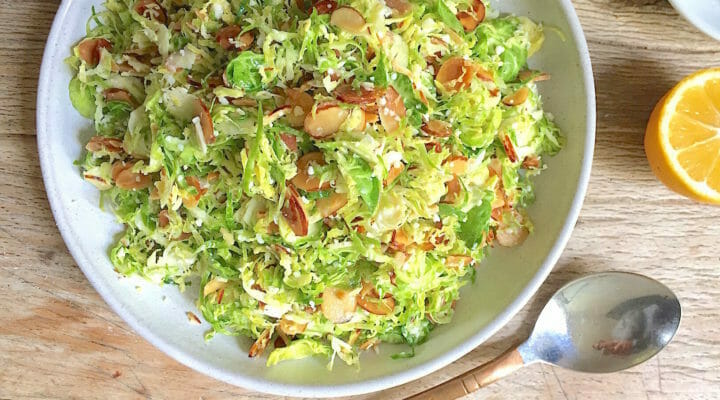 shaved brussels sprouts salad in a bowl with sliced almonds and pecorino with a spoon and a half lemon on the side