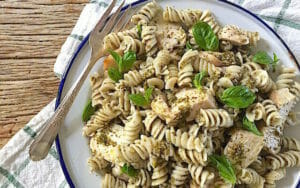 Bowl of rotini pasta with pesto and chicken with a fork
