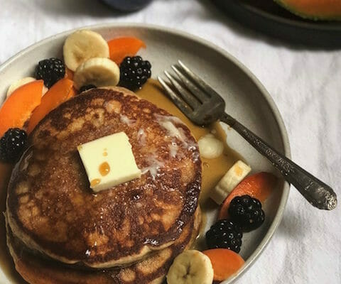 stack of whole wheat pancakes with pat of butter, apricots and other fruits