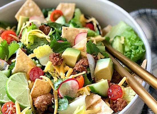 Close up of a chopped taco salad with avocado, ground meat, radishes, and limes
