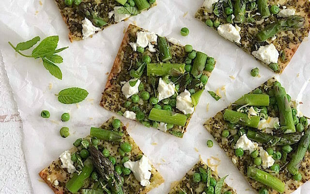 squares of pesto and asparagus pizza with goat cheese and mint on white parchment