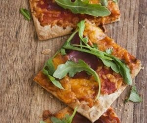 square slices of pizza with arugula on a wooden board