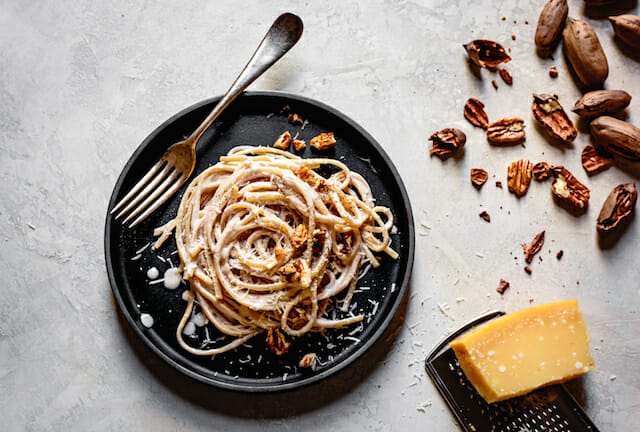 Linguine alfredo on a dark plate with a fork, parmesan, and pecans, one of 20 tasty heart healthy foods 