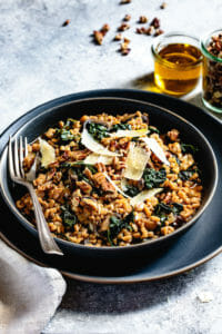 Instant Pot Farro Risotto in a black bowl with olive oil and chile flakes on the side