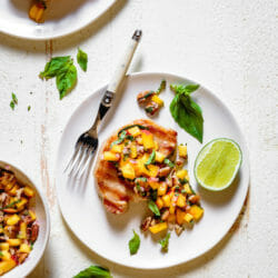 Grilled pork chop on white plate with fork and peach salsa
