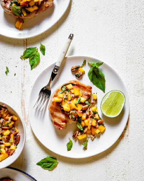 Grilled pork chop on white plate with fork and peach salsa