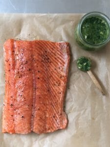 cooked salmon on parchment with a glass dish of green herb sauce