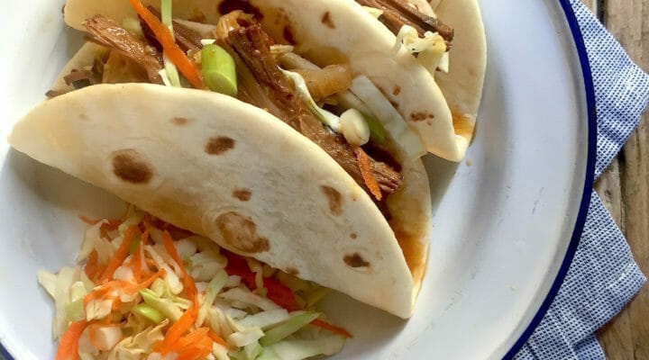 Instant Pot Korean Beef Tacos in tortillas on a plate with a blue cloth