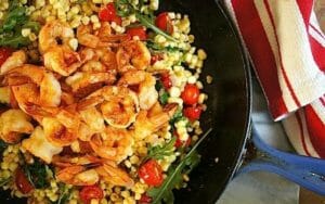 cast iron skillet with corn and shrimp with tomatoes and arugula