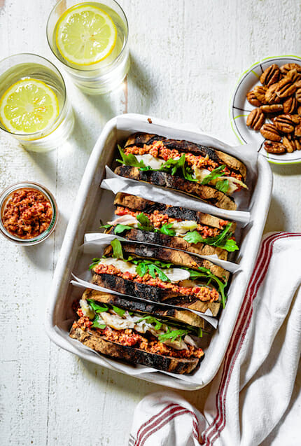 Rotisserie chicken sandwich with muhammara and arugula in white ceramic dish and water glass